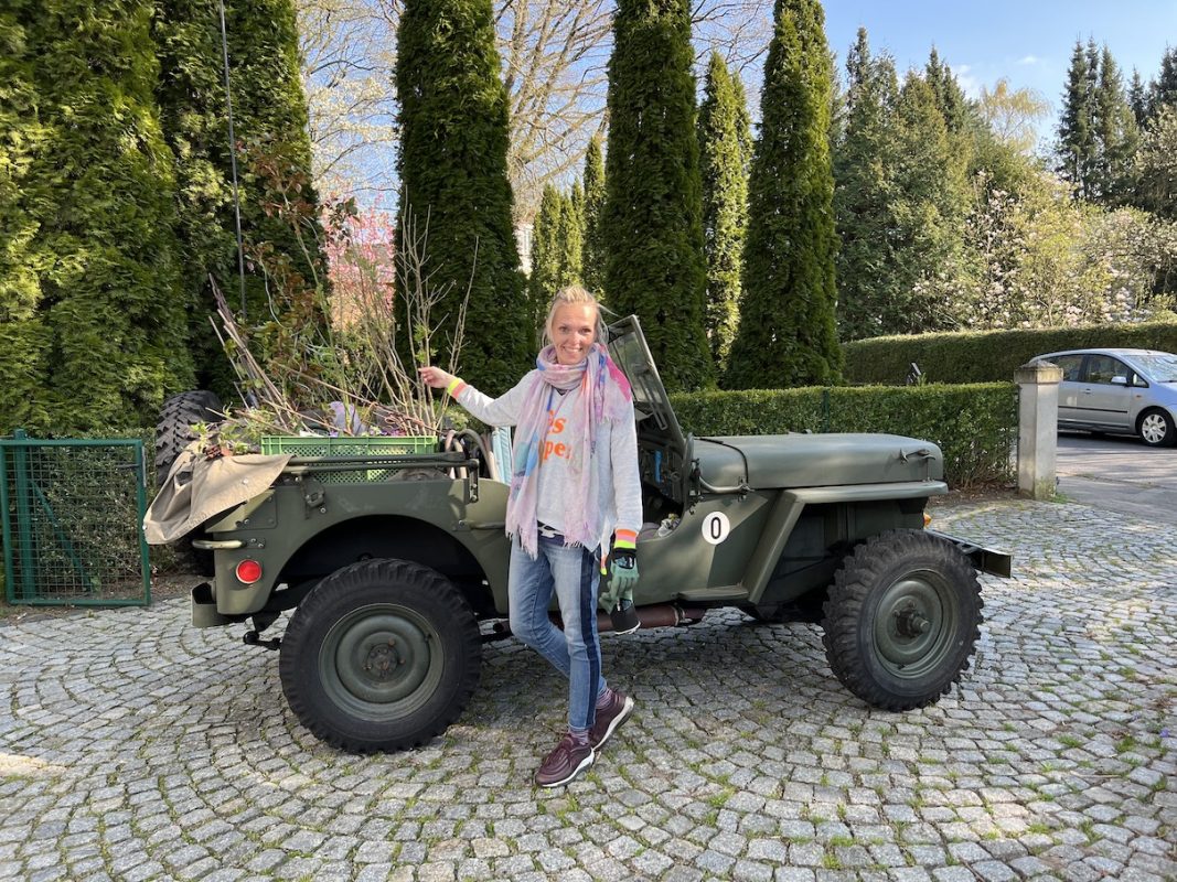 Auf dem Foto ist Nina zu sehen, wie sie ihre Blumen in einem offenen Jeep in das neue Zuhause transportiert.